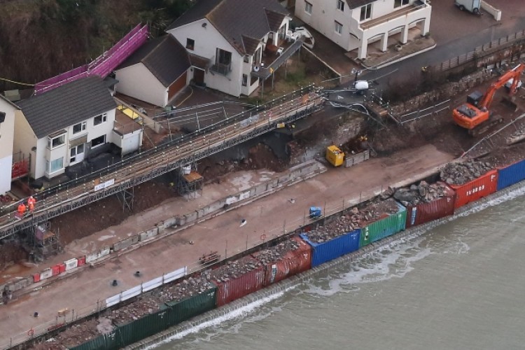 Containers filled with rocks have been used to create a temporary sea wall. Pictures below show the damage and the repair work.