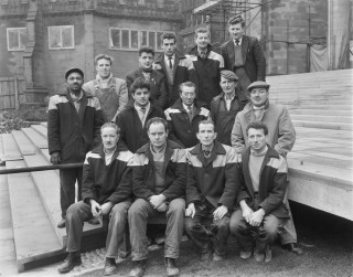 A group portrait of Laing employees who worked on the construction of Coventry Cathedral, posed on the steps leading up to the cathedral © Historic England Archive. John Laing Collection