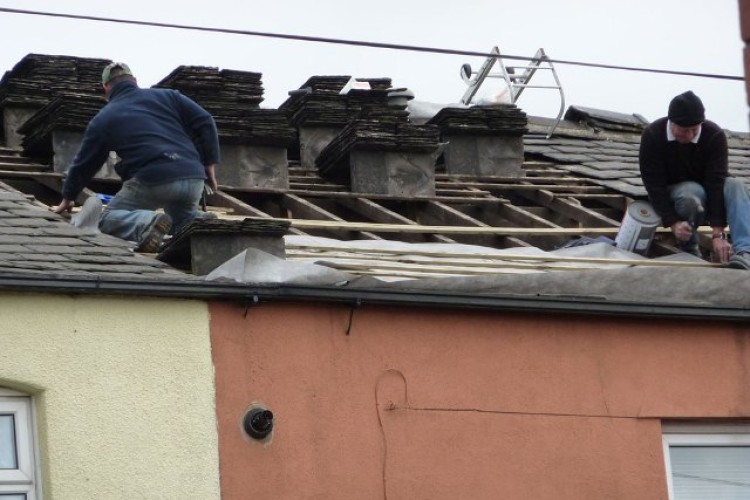 Colin Howles (right) and colleague balancing dangerously on the house roof in Oldham