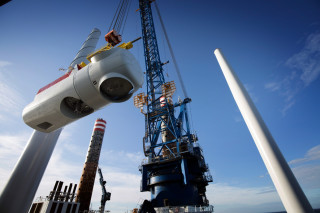 A nacelle, which houses the generator, and transformer is lifted onto the top of a turbine tower.