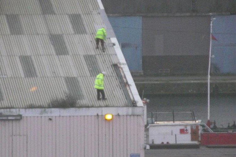 Workers on a sloping warehouse roof in Birkenhead without safety measures in place
