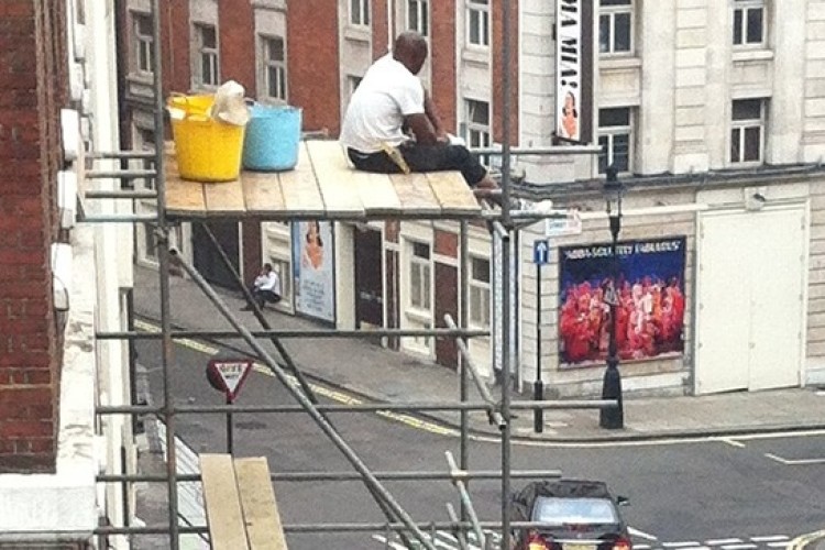 A worker sits on boarding with no guard rails, harness or other measures in place